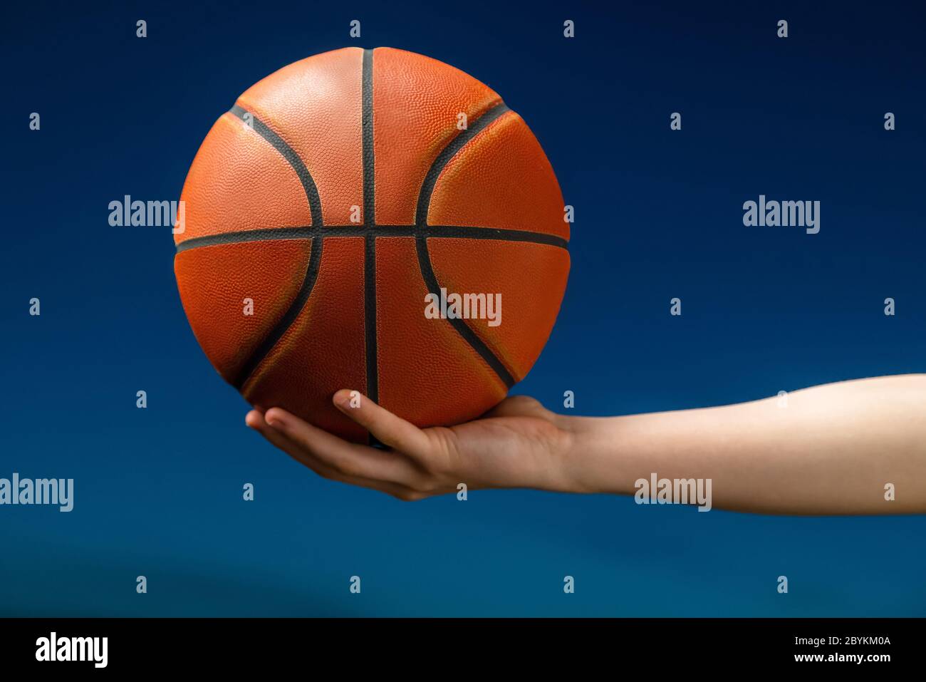 Nahaufnahme eines professionellen Basketballspielers, der einen Ball in der Hand hält. Street Basketball-Athlet mit einem Ball und blauen Himmel im Hintergrund Stockfoto