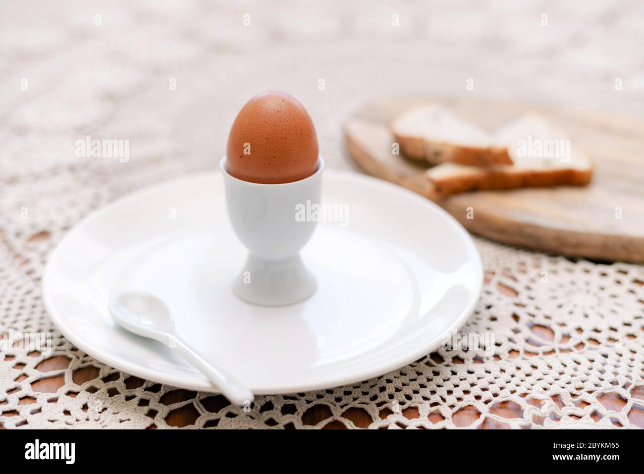 Leckeres gekochtes Ei in einer Tasse mit knusprig geröstetem Brot zum Frühstück. Gesundes Essen auf dem Küchentisch. Stockfoto