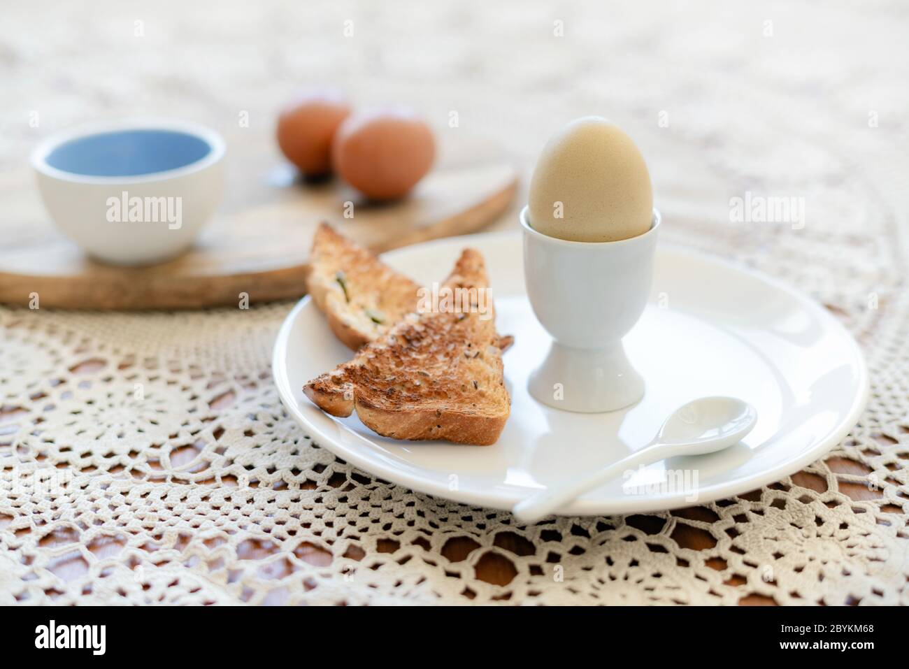 Leckeres gekochtes Ei in einer Tasse mit knusprig geröstetem Brot zum Frühstück. Gesundes Essen auf dem Küchentisch. Stockfoto