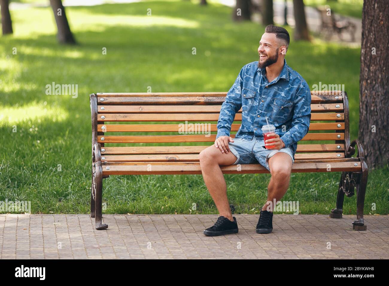 Ein Mann mit Limonade ruht im Frühjahr in einem Park auf einer Bank. Sonniger Tag. Stockfoto