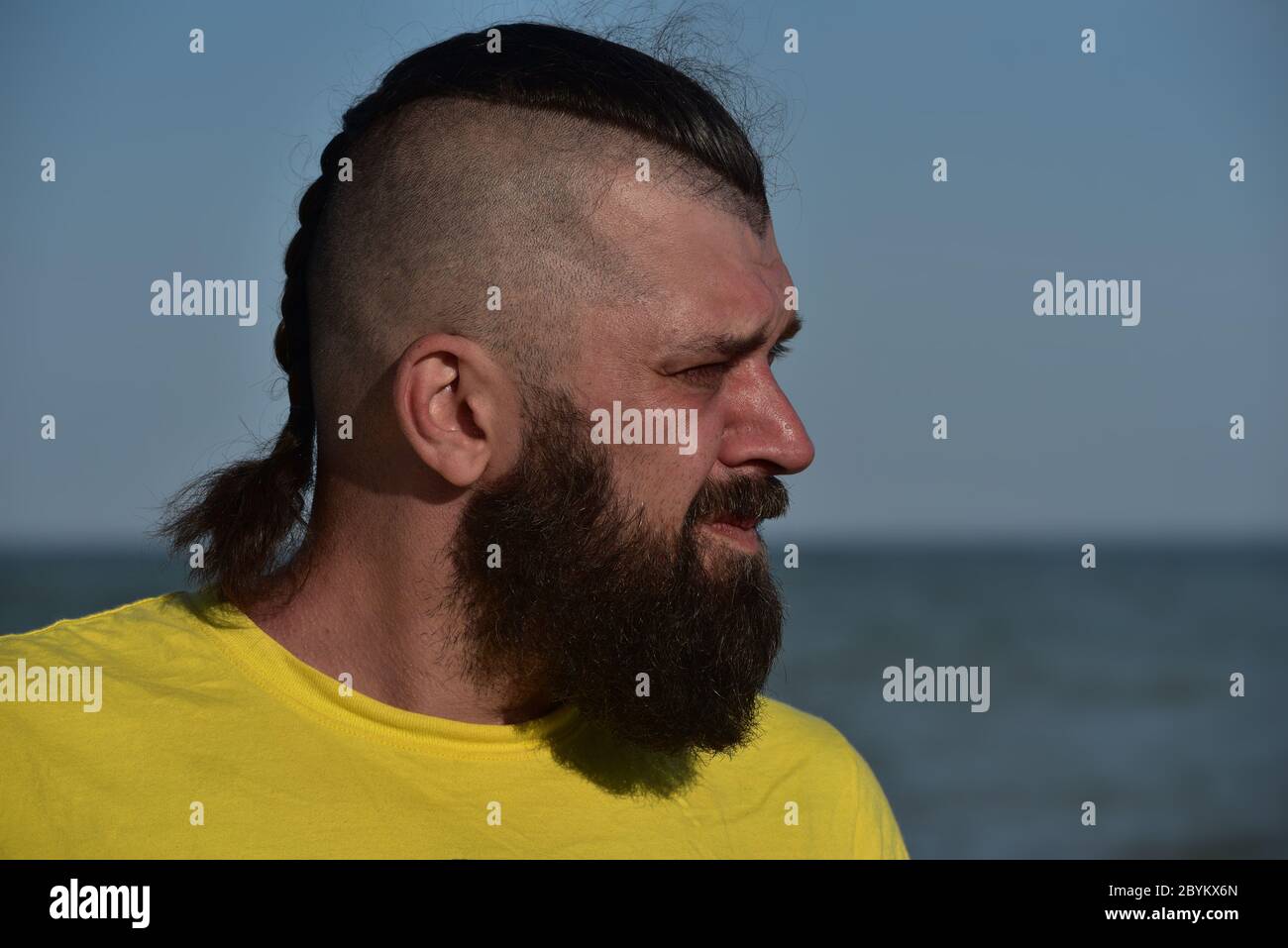 Ein junger Mann, der ein gelbes T-Shirt und Shorts trägt. Mann in einem gelben T-Shirt mit Bart auf dem Hintergrund des Meeres. Stockfoto