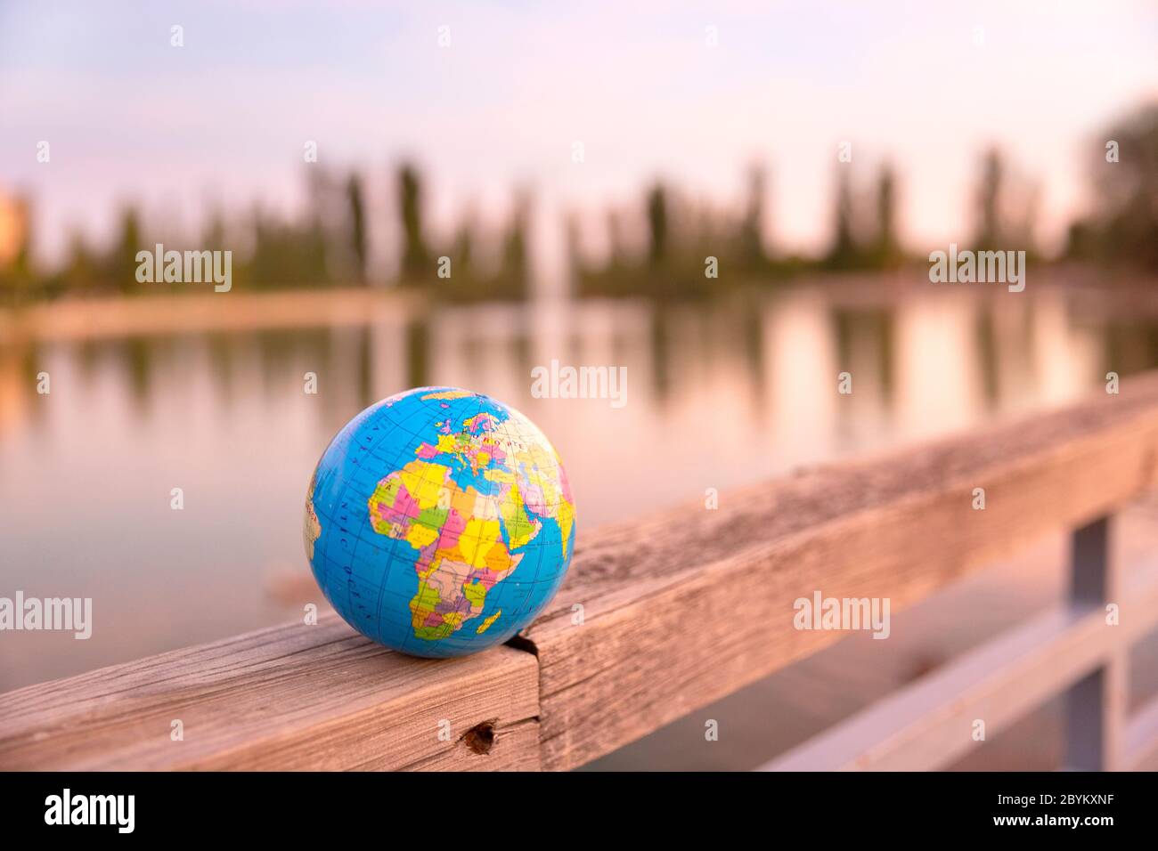 Kleine Weltkugel, die auf dem hölzernen Zaun eines großen Sees aufgestellt wird. Reisekonzept und Pflege des Planeten. Stockfoto