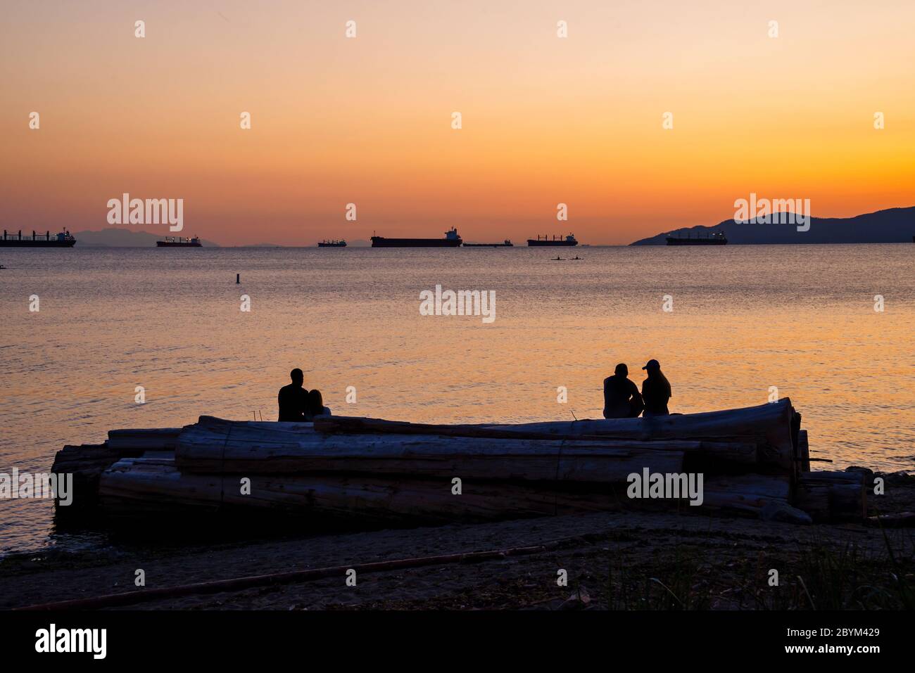 Silhouetten von Menschen, die den Sonnenuntergang im Sommer am English Bay Beach in Vancouver, British Columbia, Kanada genießen Stockfoto