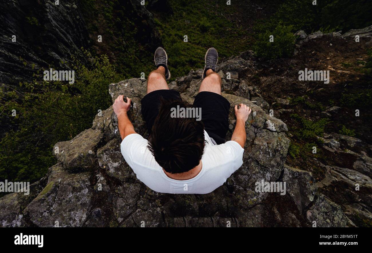 Mann auf dem Rand eines Felsens, Blick auf seine Füße. Luftaufnahme Reise Lifestyle Abenteuer Urlaubskonzept Stockfoto