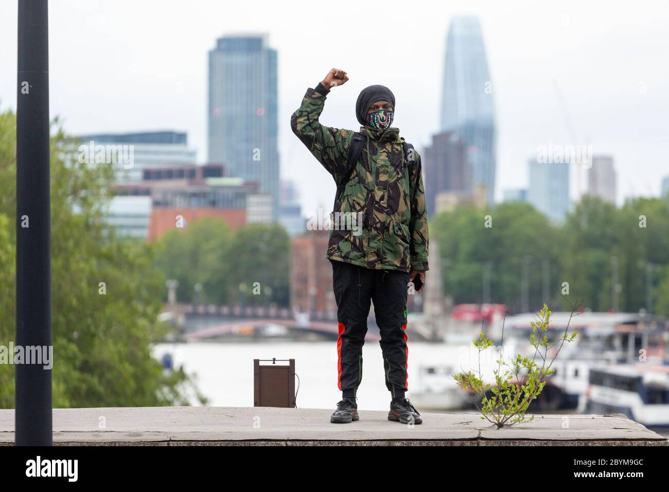 Ein Mann in einer Armeejacke steht auf der Vauxhall Bridge mit der Faust, die während eines Black Lives Matters Protests in London am 7. Juni 2020 erhoben wurde Stockfoto