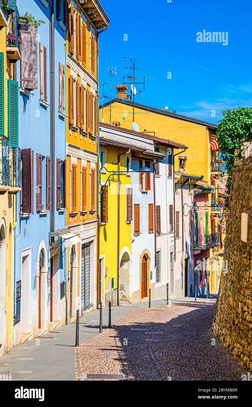 Typische schmale Straße in der Altstadt von Desenzano del Garda Stadt mit Kopfsteinpflaster Straße und traditionellen bunten Gebäuden mit Fensterläden, vertikale Ansicht, Lombardei, Norditalien Stockfoto