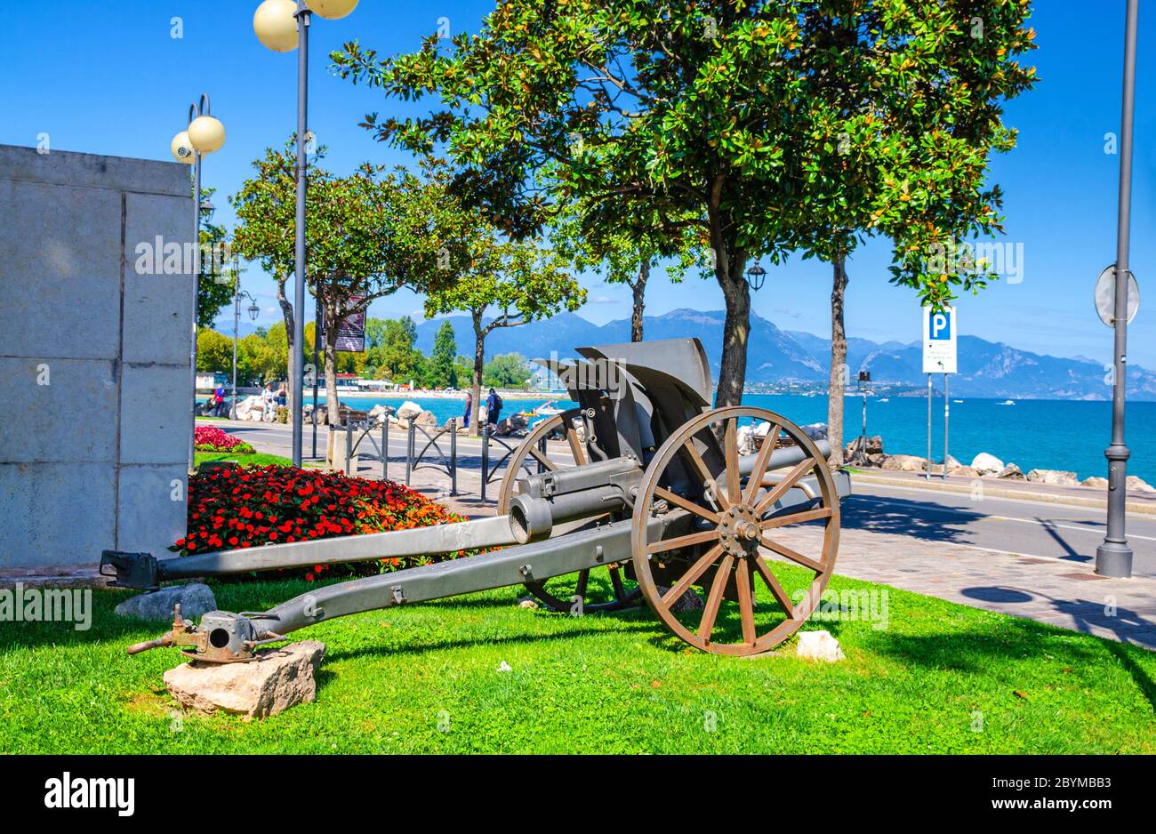 Kanone auf grünem Rasen im historischen Zentrum von Desenzano del Garda Stadt mit Blick auf Gardasee Promenade Böschung und Bergkette, blauer Himmel Hintergrund, Lombardei, Norditalien Stockfoto