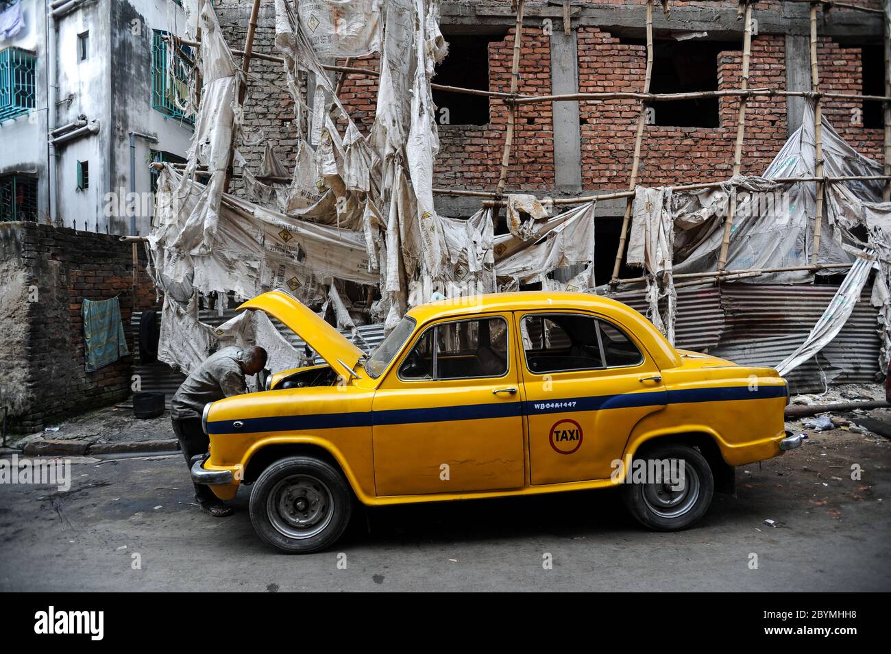 03.12.2011, Kalkutta, Westbengalen, Indien - EIN Taxifahrer schaut unter die Haube seines gelben Hindustan Ambassador Taxis. Der Botschafter war das erste ca. Stockfoto