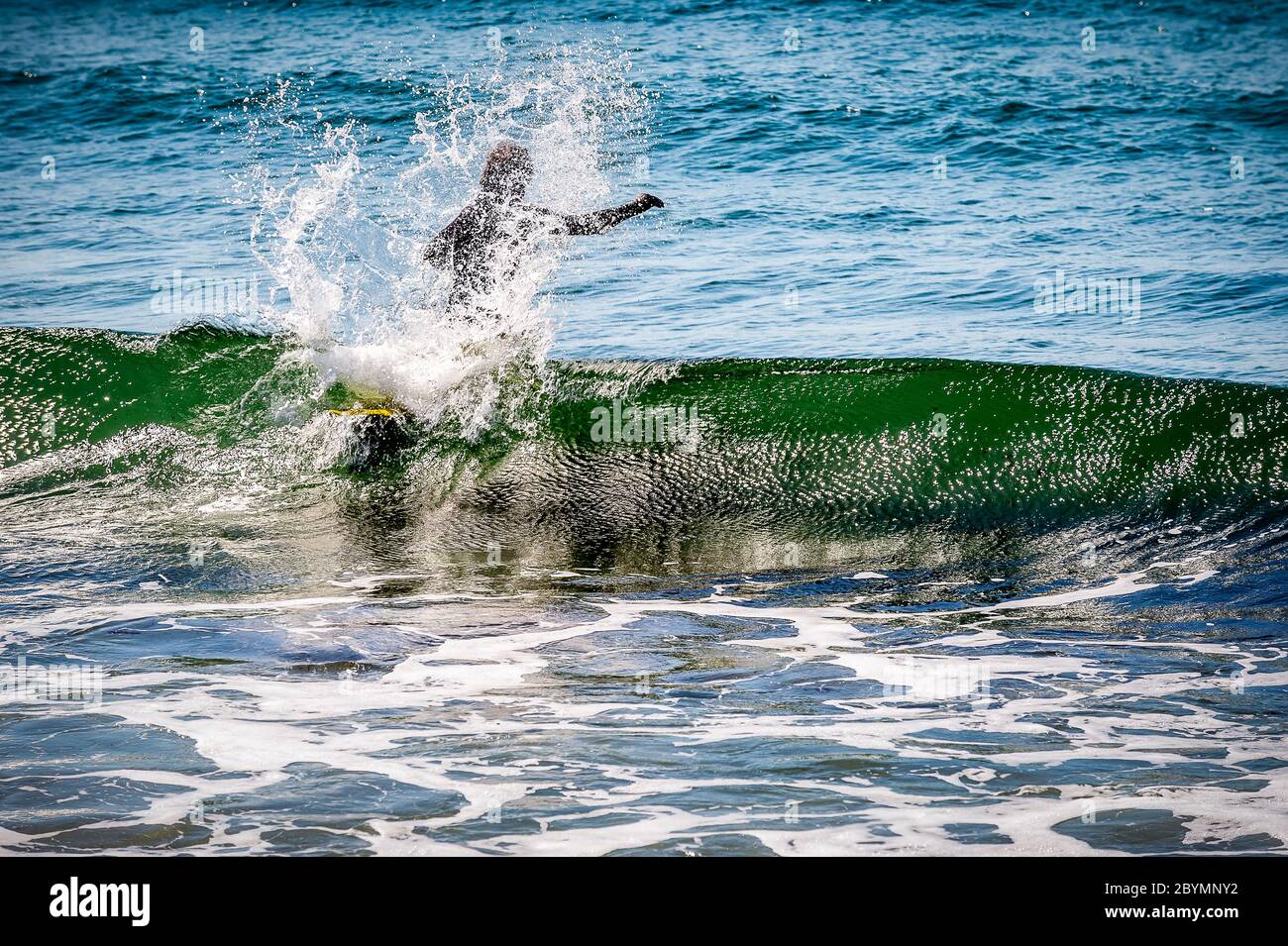 Ein Surfer macht sich auf den Kopf, um ein paar Wellen zu fangen und einen lustigen Tag außerhalb des Hauses und einen Tag ohne Maske zu haben.aber in diesem Fall fing die Welle den Surfer, Stockfoto
