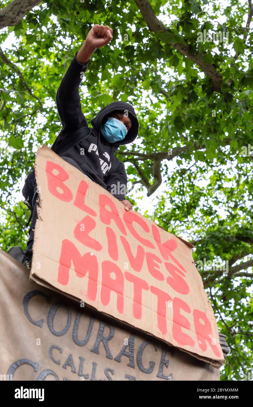 Ein junger schwarzer Protestler sitzt während eines Black Lives Matters Protestes auf dem Parliament Square, London, 7. Juni 2020, auf einer Statue von Millicent Fawcett Stockfoto