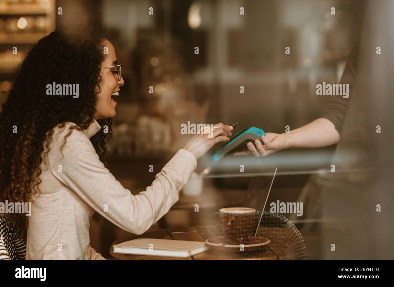 Lächelnde Frau, die mit NFC-Technologie in einem Café bezahlt, um ihre Rechnung zu bezahlen. Weibliche Kundin, die ihre Rechnung mit einem Smartphone und einem elektronischen Lesegerät bei c bezahlt Stockfoto