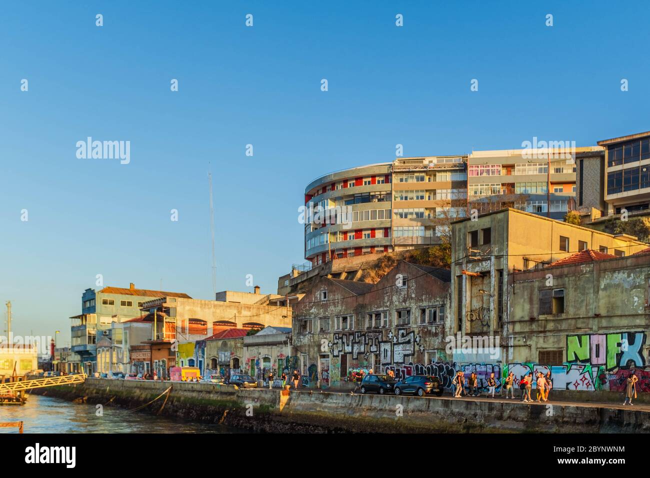 Menschen, die bei Sonnenuntergang in Almada an alten, verlassenen und mit Graffiti bedeckten Fabriken vorbei gehen. Stockfoto