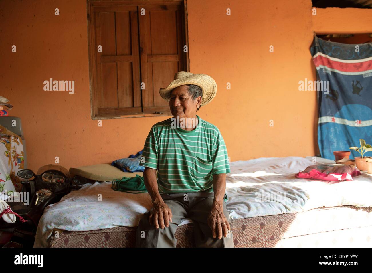 Portrait des Latino-Mannes, der nach der Siesta auf dem Bett sitzt (Mittagsschlaf). Alltag in El Paredón, Guatemala. Dezember 2018 Stockfoto