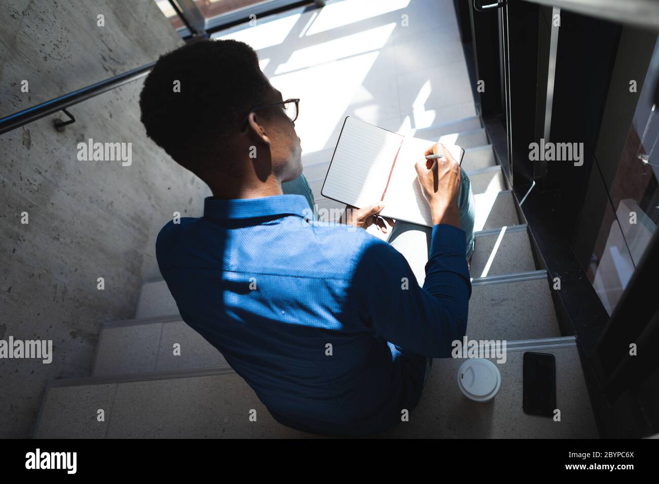 Afroamerikanischer Mann sitzt auf Treppen und schreibt in einem Notizbuch Stockfoto