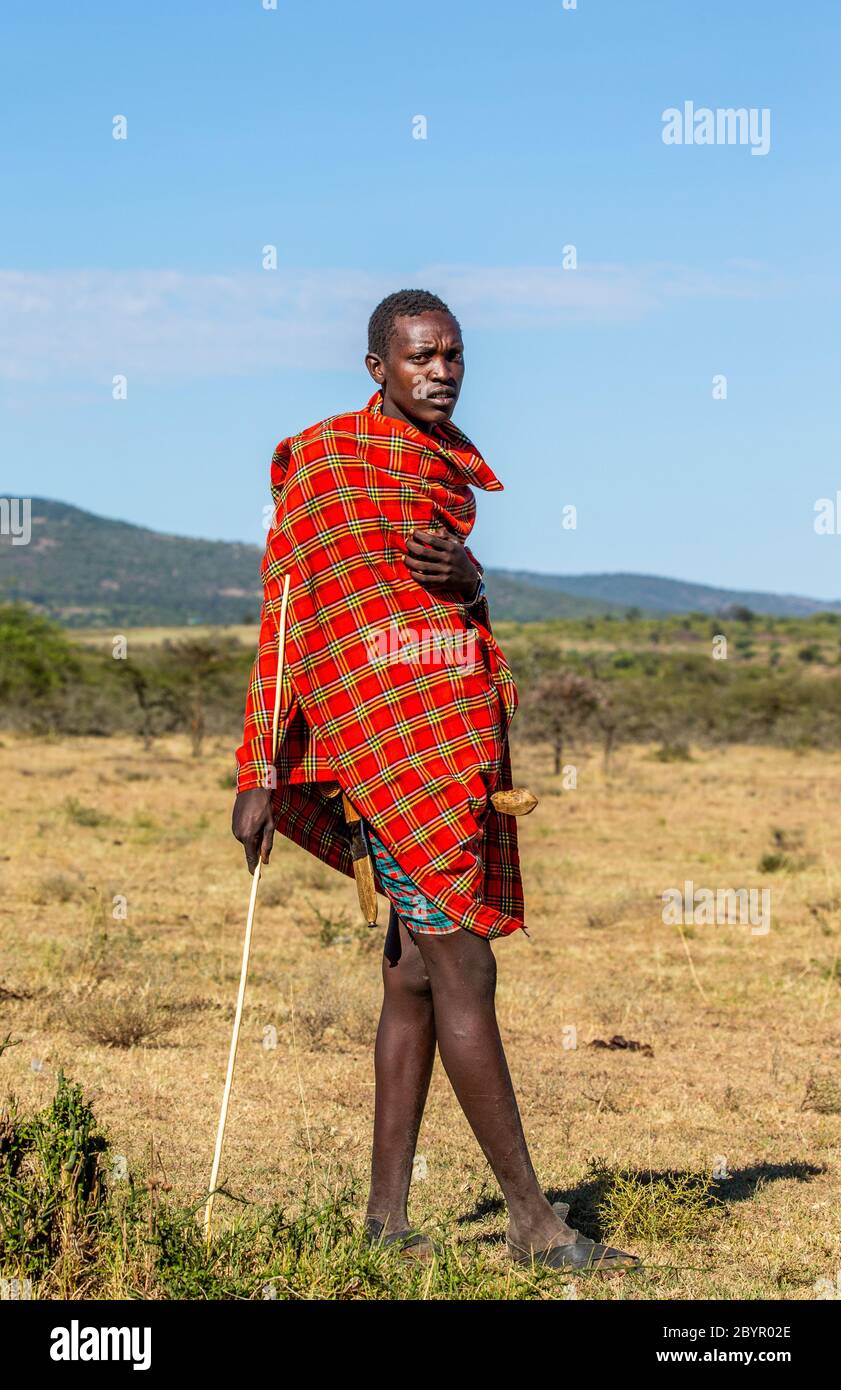 Masai Mann in traditioneller Kleidung steht in der Savanne. Tansania, Ostafrika, 12. August 2018. Stockfoto