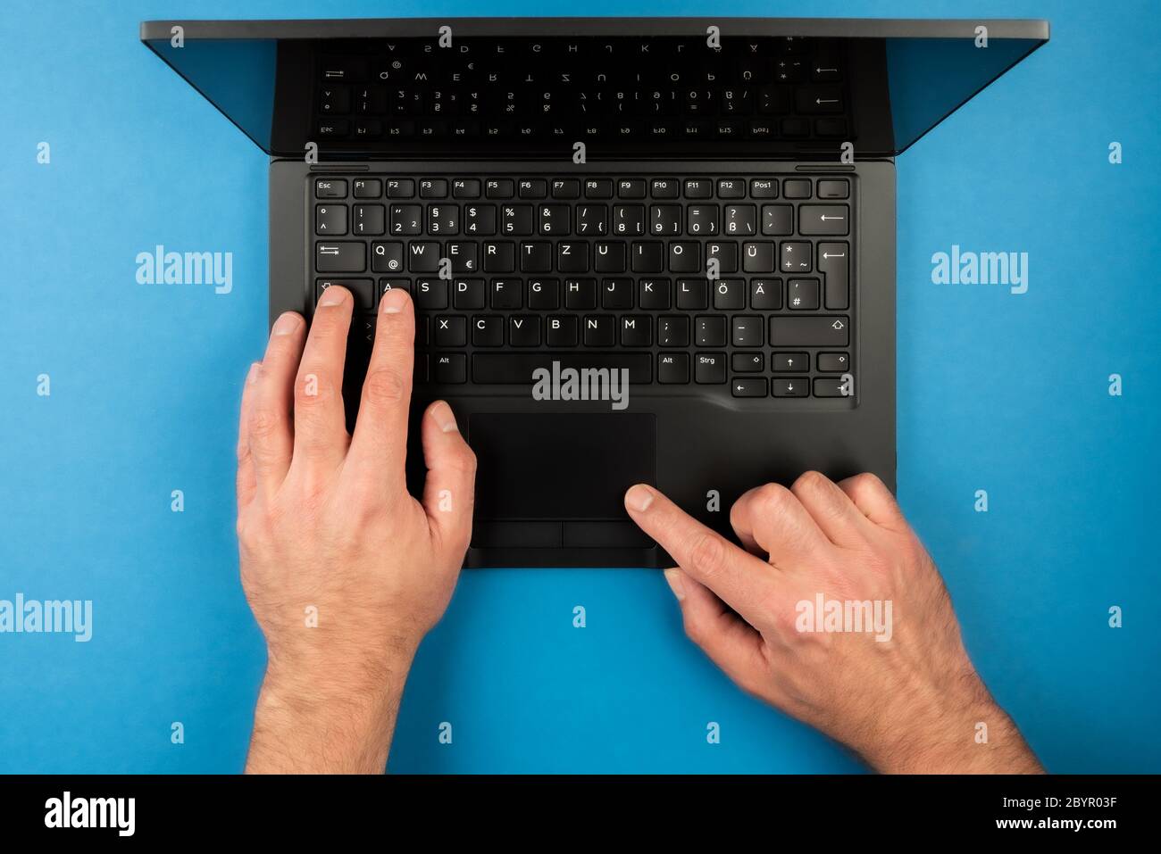 Direkt über der Ansicht des Mannes mit Laptop-Computer auf blauem Schreibtisch Hintergrund Stockfoto