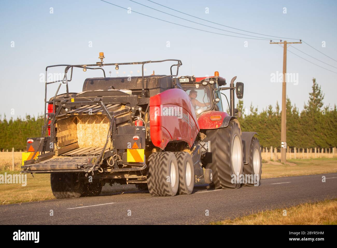 Annat, Canterbury, Neuseeland, Februar 10 2020: Ein roter Farmtraktor mit roter Heupresse fährt auf einer Landstraße Stockfoto