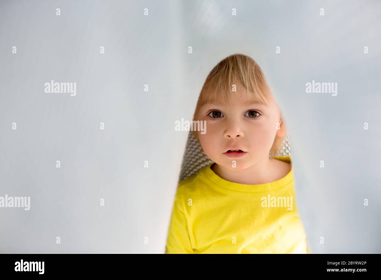 Kleiner kleiner kleiner kleiner Junge mit gelbem Hemd, versteckt unter Decke, lächelnd glücklich Stockfoto