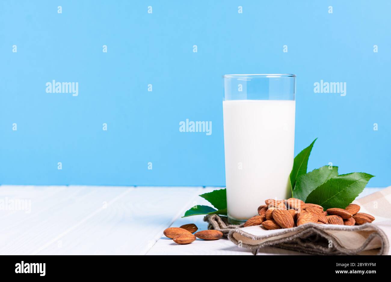 Laktosefreies Milchkonzept, Glas mit Mandelmilchnüssen auf weißem Tisch auf blauem Hintergrund Stockfoto