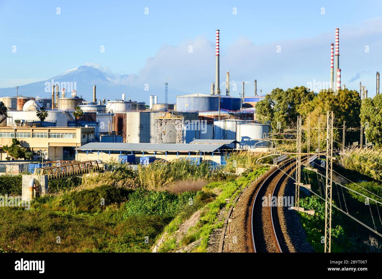 Eisenbahn durch das Enel-Kraftwerk zwischen Catania und Syrakus, Sizilien, Italien, während der Ätna ausbricht Stockfoto