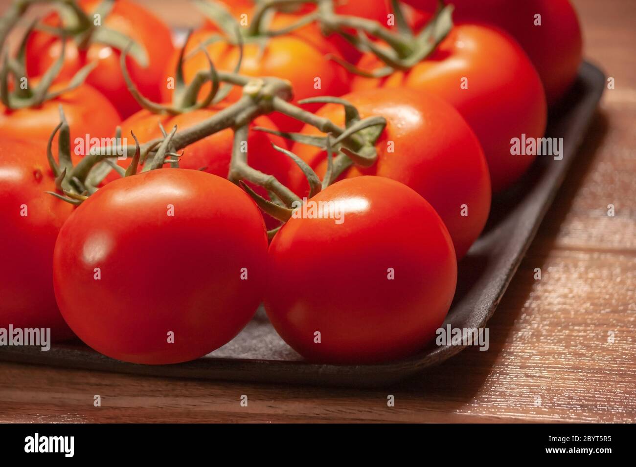 Viele frische reife Tomaten mit Stiel in schwarzem Tablett aus dem Supermarkt Stockfoto