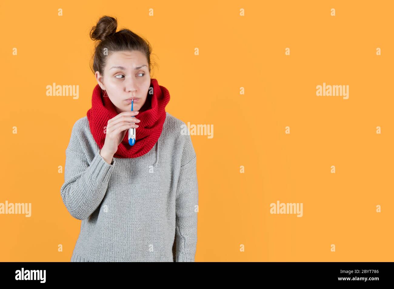 Mädchen in einem Pullover hält ein elektronisches Thermometer in ihr Mund und schaut weg Stockfoto