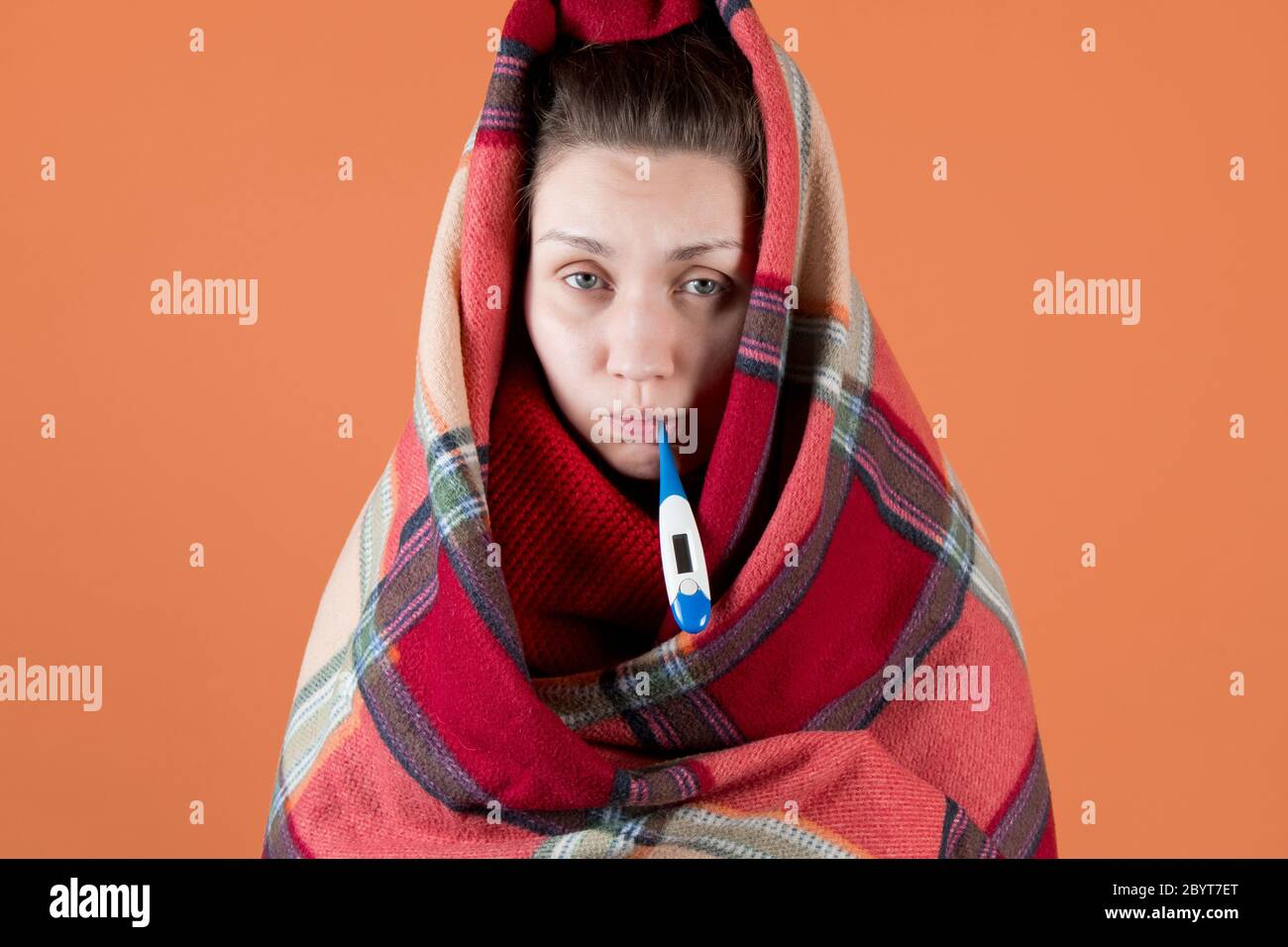 Das kranke Mädchen wickelte sich in ein Karli und hält Ein Thermometer in ihrem Mund Stockfoto