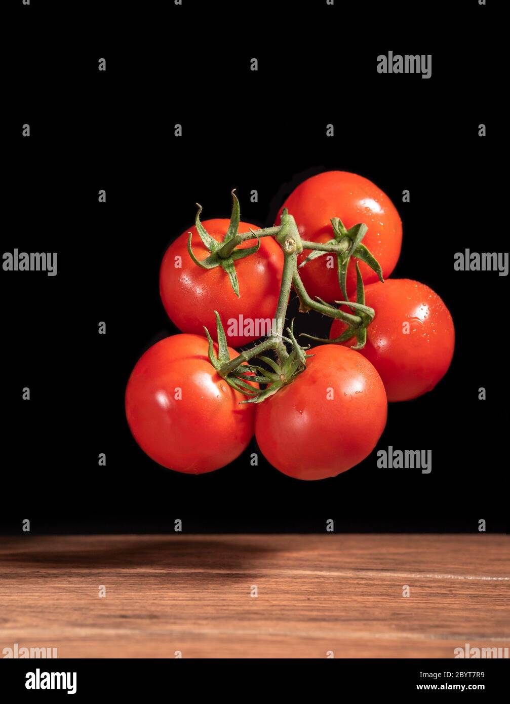 Bouquet von Bio-roten Tomaten fallen in einen Holztisch mit schwarzem Hintergrund Stockfoto