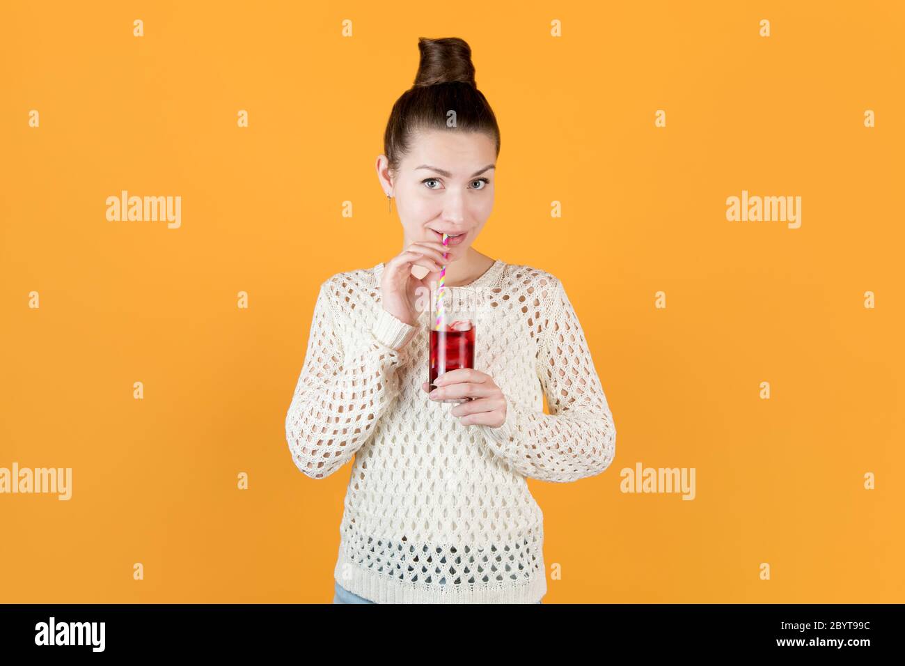 Mädchen trinkt Kirschsaft aus einem gestreiften Stroh und sieht hintangend aus. Stockfoto