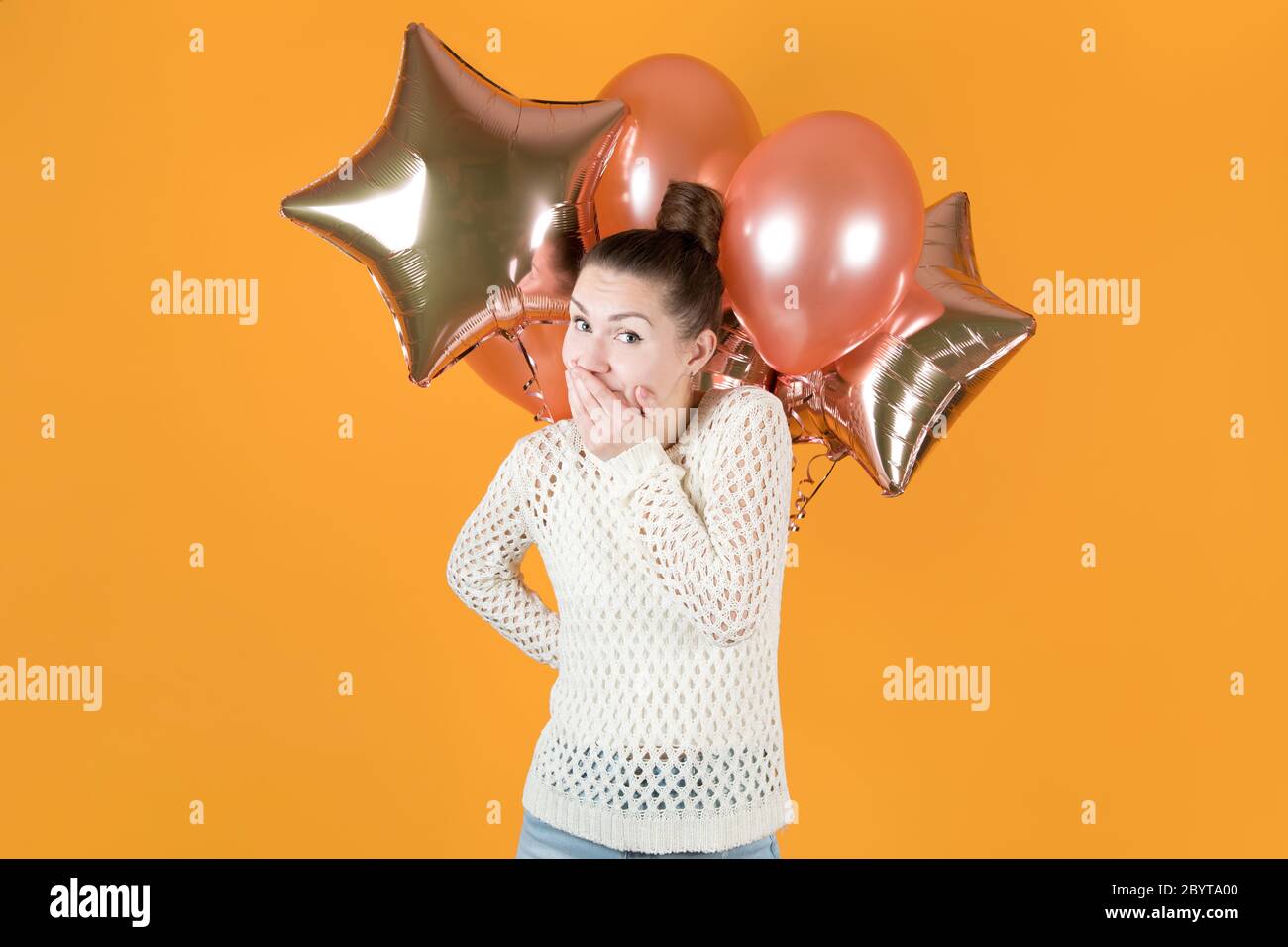 Das Mädchen hält verschwörerisch Lachen zurück und hält festliche Ballons hinter sich Stockfoto