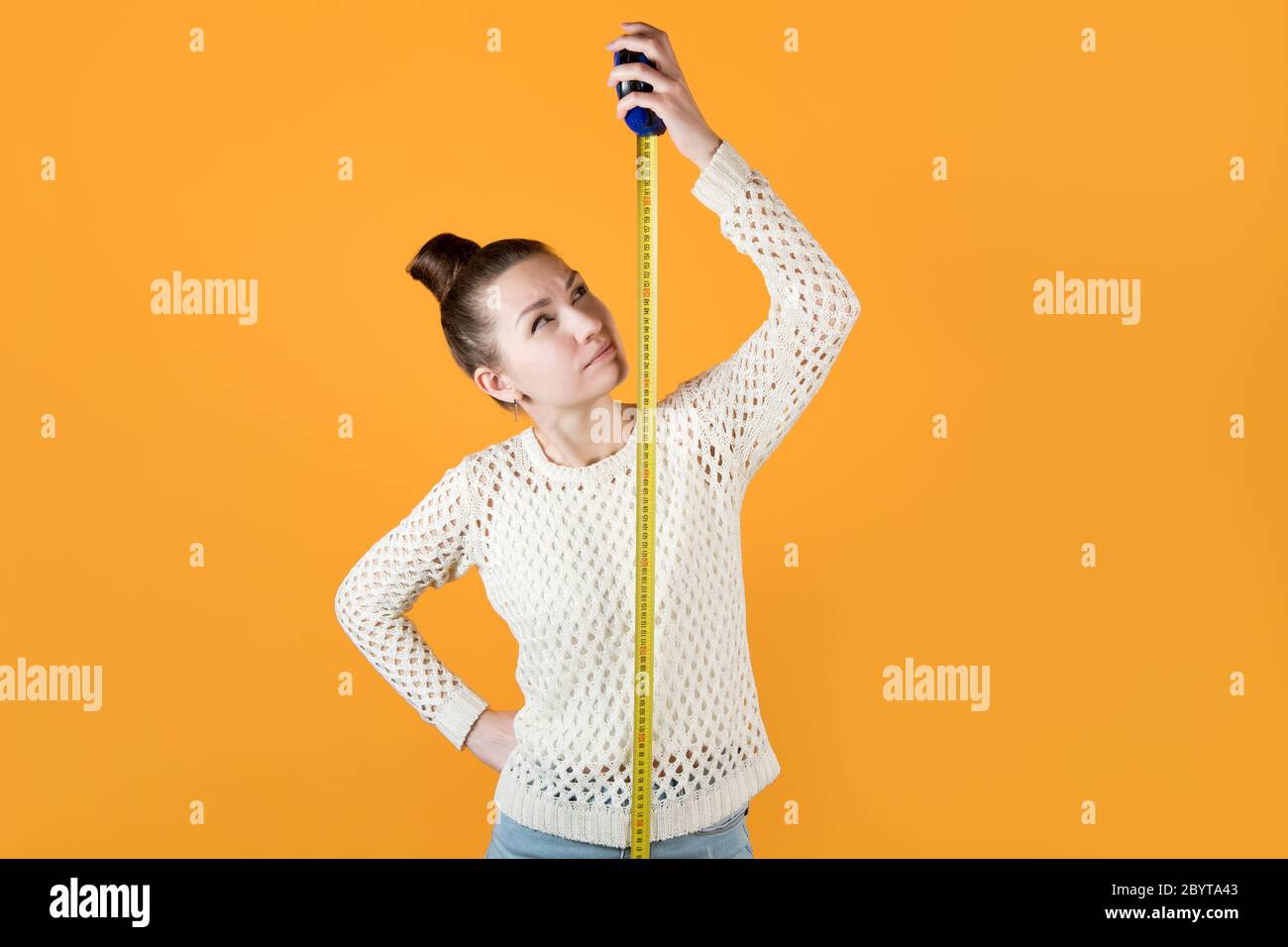 Mädchen sieht verdächtig auf ein Maßband neben ihr gespannt Stockfoto