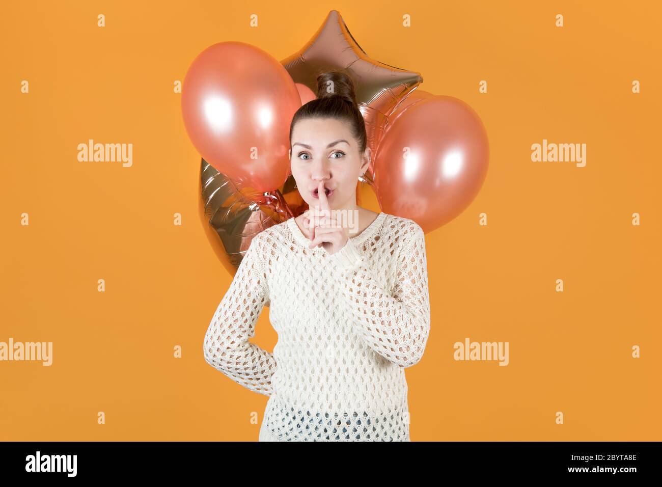 Mädchen bedeckt ihren Mund mit einem Finger Drängen zu schweigen und hält festliche Ballons hinter ihr Stockfoto