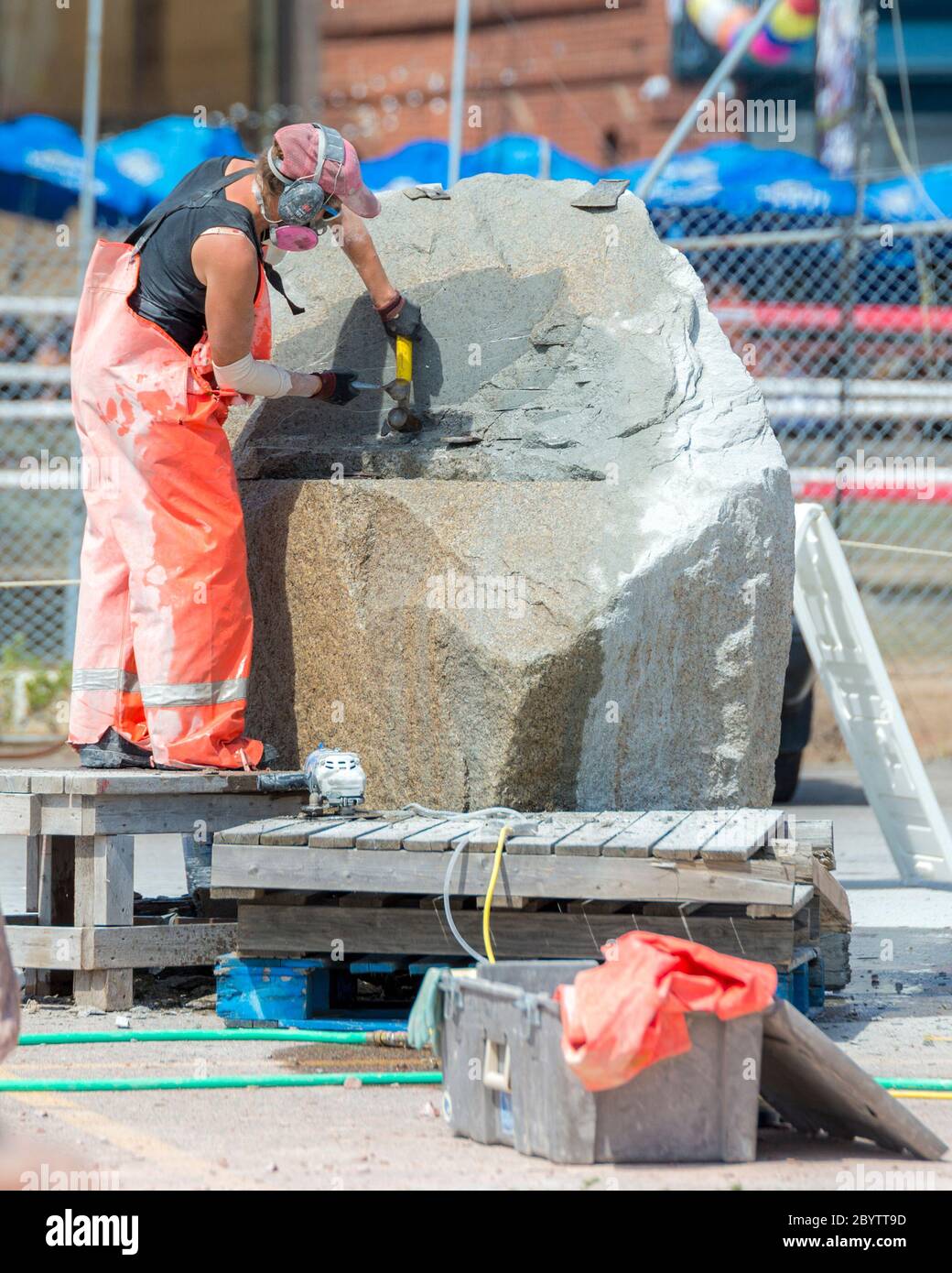 Ein Künstler arbeitet an einem großen Steinblock im Sculpture Saint John, einem Skulpturensymposium, das Künstler aus aller Welt beherbergt. Stockfoto