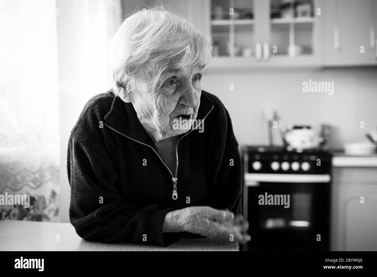 Eine alte Frau in der Küche am Fenster in seinem Haus. Schwarzweiß-Foto. Stockfoto