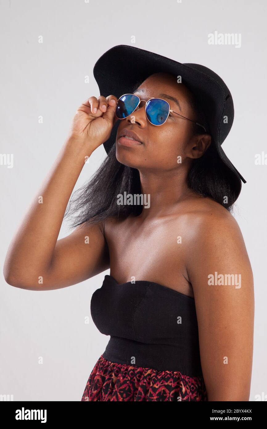 Hübsche schwarze Frau in Sonnenbrille und schwarzem Hut Stockfoto