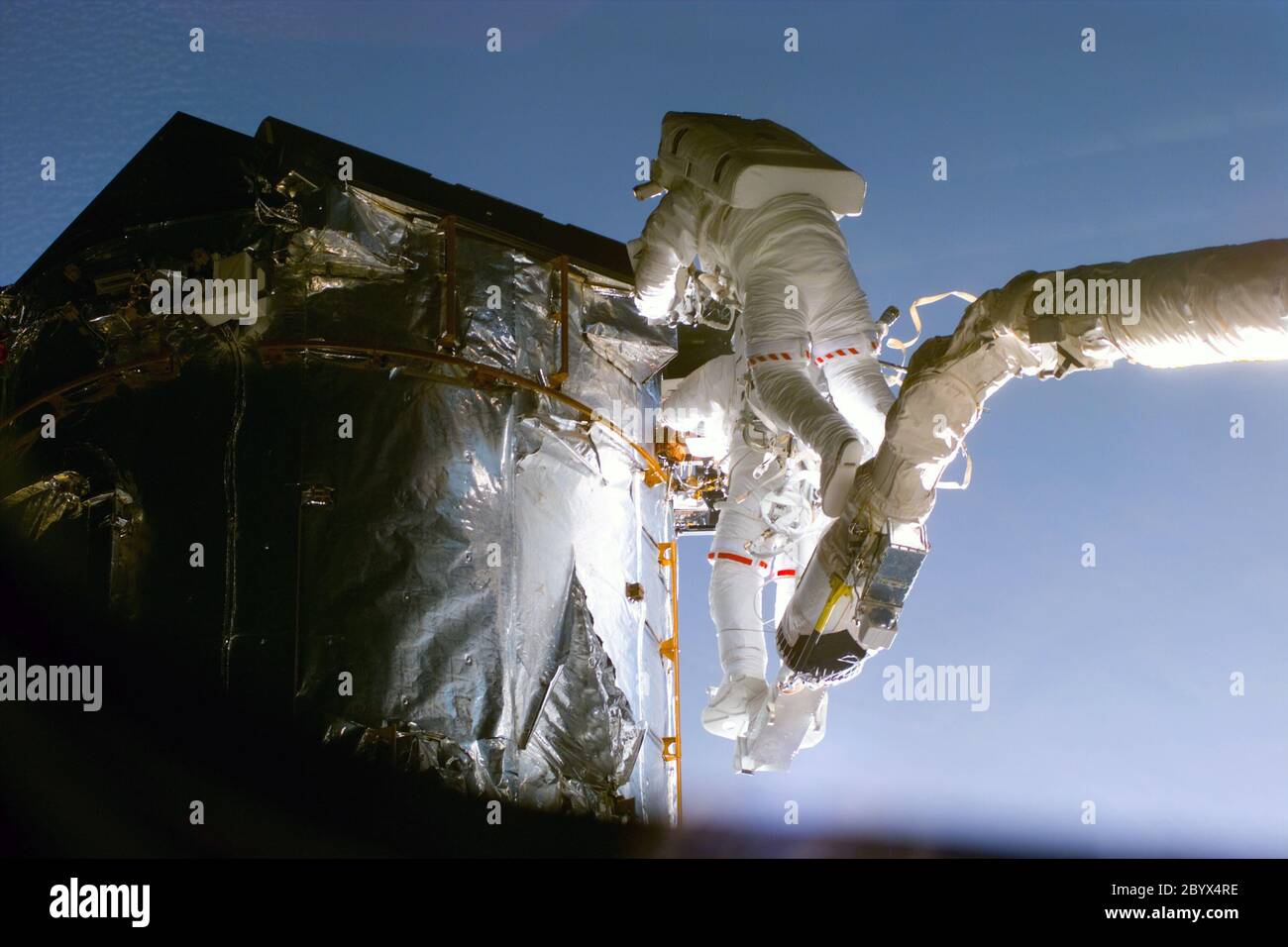 S82-E-5652 (17. Februar 1997) --- Astronaut Gregory J. Harbaugh (Solid Stripe on EMU) verwendet Remote Manipulator System (RMS) als Cherry-Picker-Gerät, um Hubble Space Telescope (HST) zu warten. In Zusammenarbeit mit dem Astronauten Joseph R. Tanner in der Nähe war der Missionsspezialist dabei, die Schutzkappen des Magnetic Sensing System (MSS) der HST durch neue, dauerhafte Abdeckungen zu ersetzen. Diese Ansicht wurde mit einer elektronischen Standkamera (ESC) aufgenommen. Stockfoto