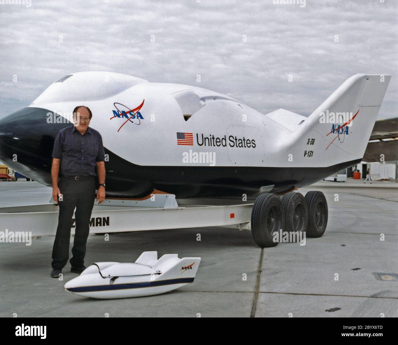 Dale Reed, ein NASA-Ingenieur, der in den 1960er und 1970er Jahren an den ursprünglichen Hubkörper-Forschungsprogrammen arbeitete, steht mit einem Scale-Modell X-38, das in 1995 Forschungsflügen eingesetzt wurde, mit einem X-38 im Maßstab 1:1 (80 Prozent der Größe eines potenziellen Crew Return Vehicle) hinter ihm. Stockfoto