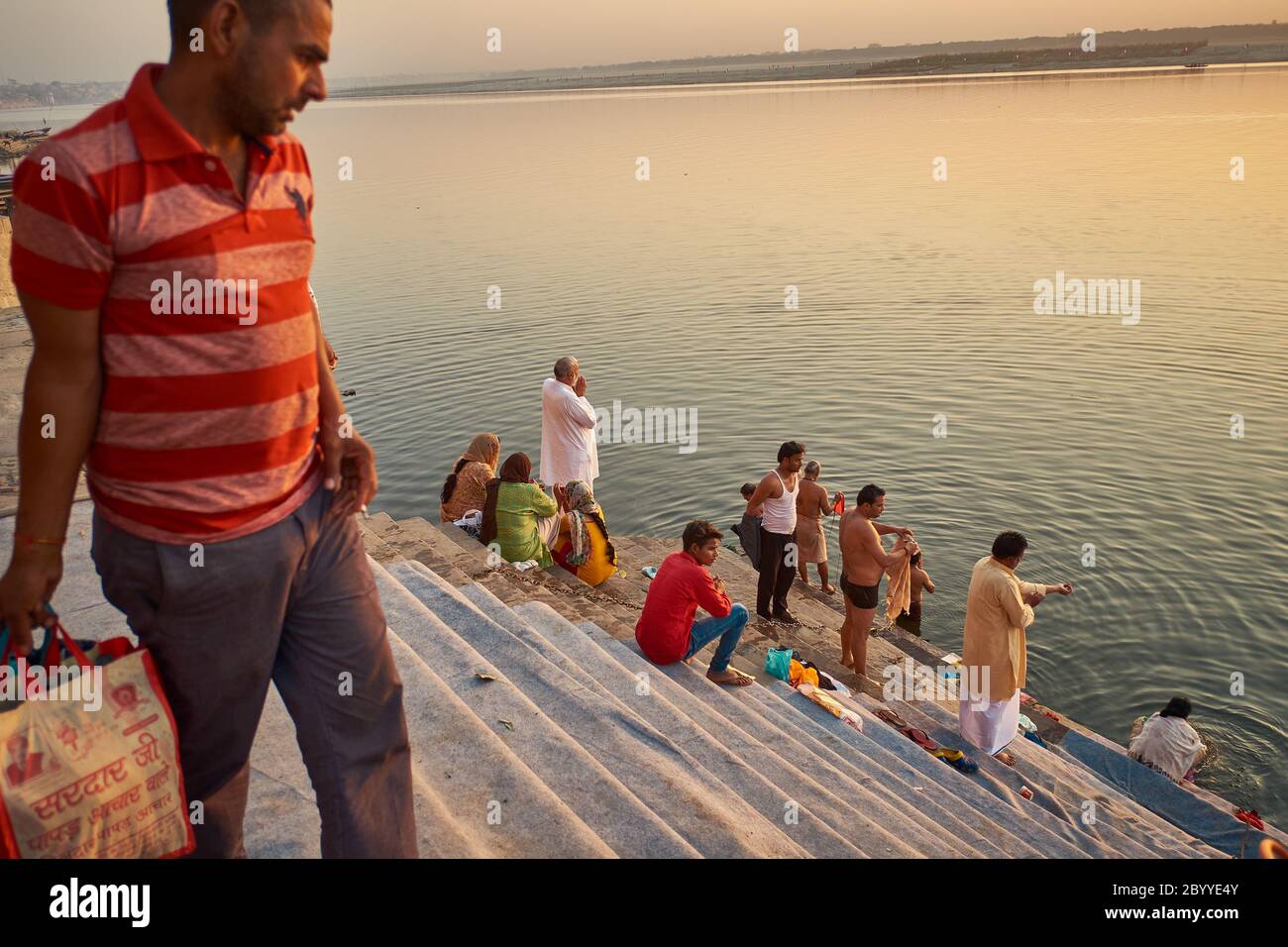 Eine Frau mittleren Alters sitzt mit ihrem Freund und betrachtet, während eine jüngere Frau ein Foto der aufgehenden Sonne am Riva Ghat, Veranasi, macht Stockfoto