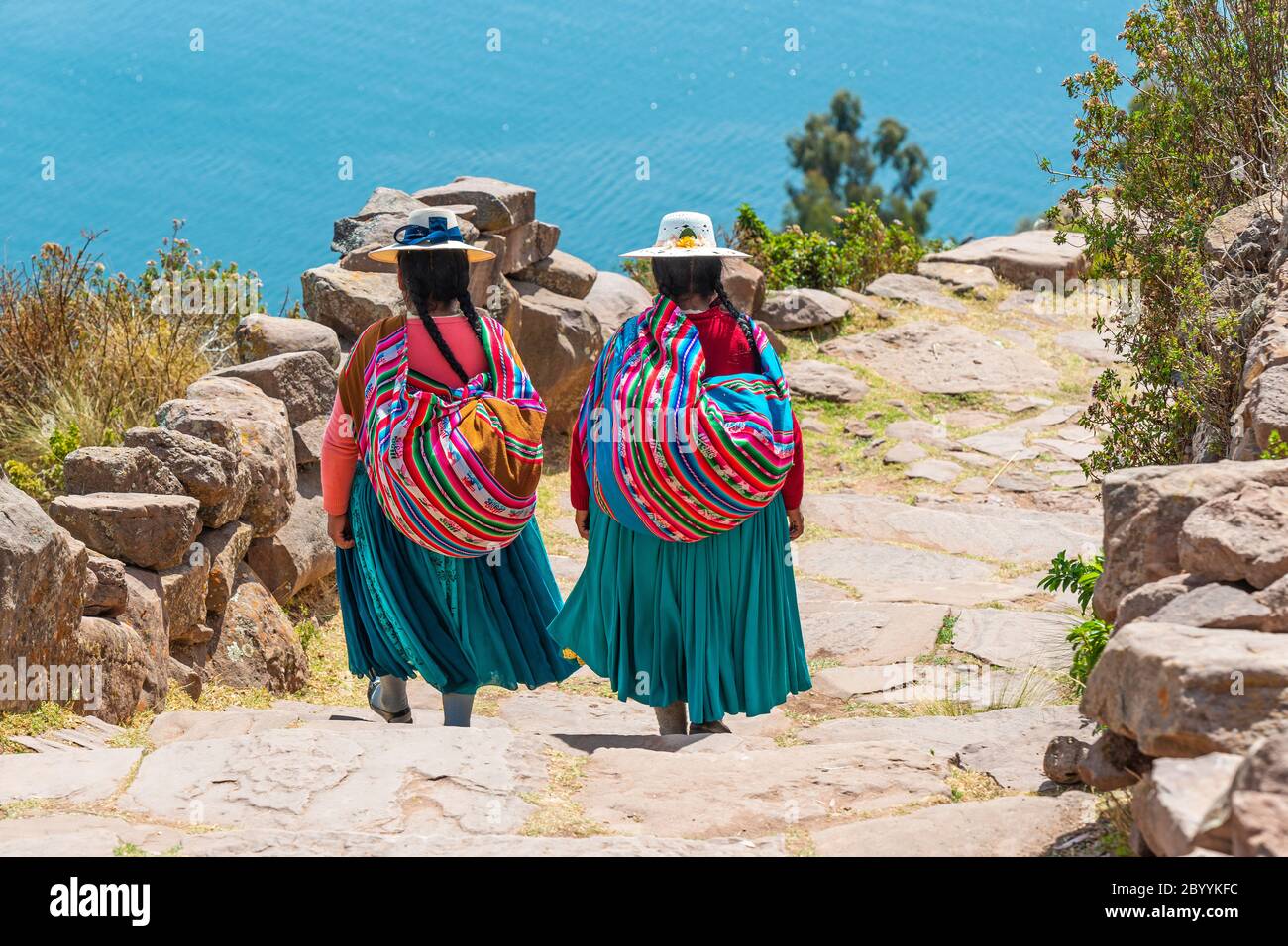 Zwei einheimische peruanische Quechua-Frauen in traditioneller Kleidung gehen die Treppe hinunter zum Hafen der Taquile-Insel, Titicaca-See, Peru. Stockfoto