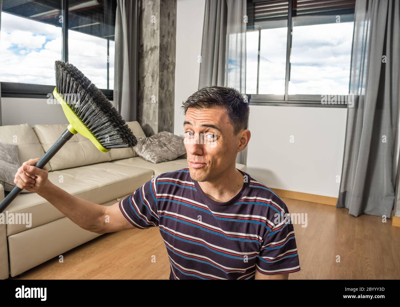 Mann in legerer Kleidung fegen sein Wohnzimmer. Mittlerer Schuss. Stockfoto