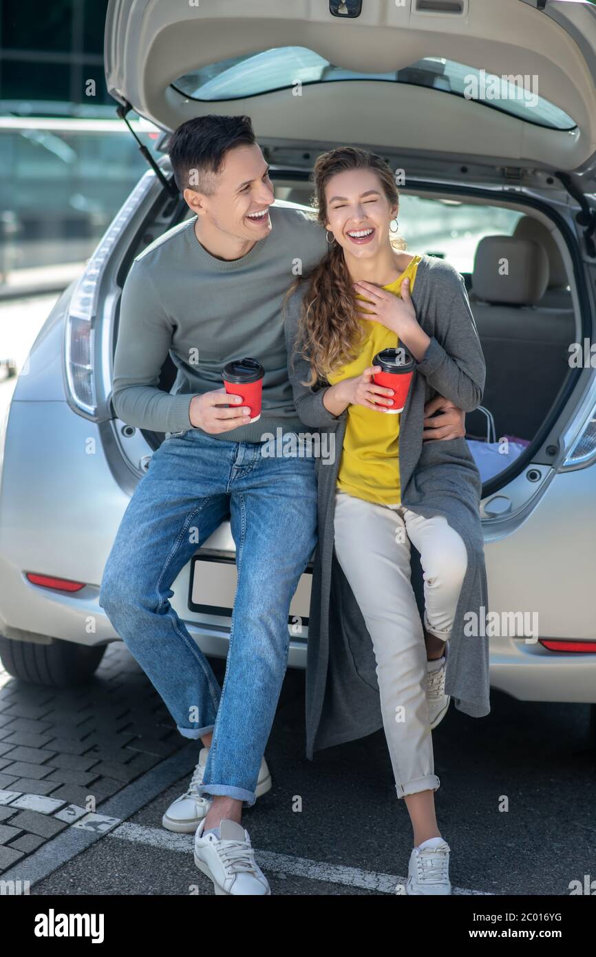 Junge schöne Mann und Frau trinken Kaffee in der Nähe eines Autos Stockfoto