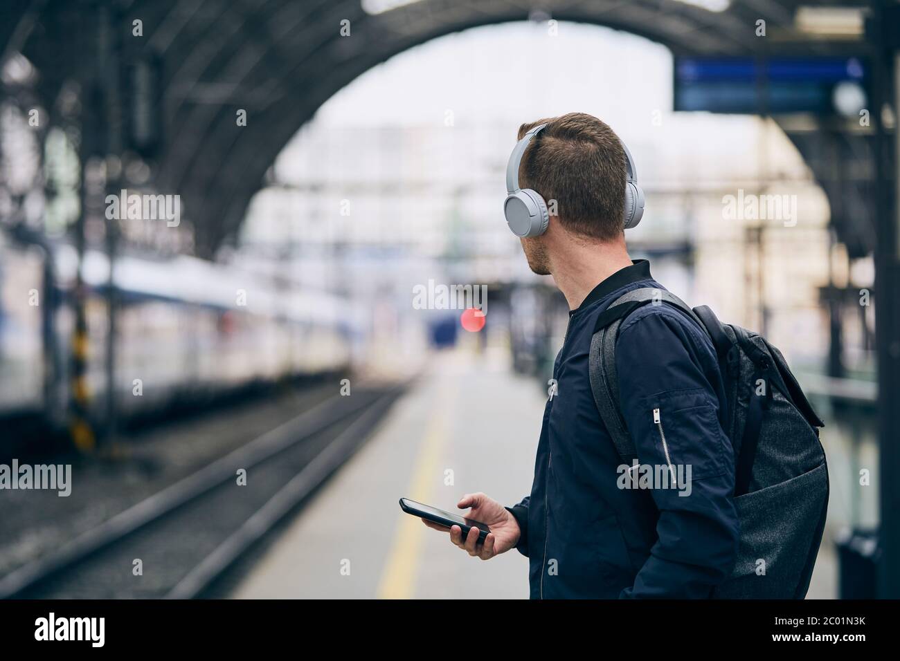 Junger Mann mit Kopfhörern, der Musik hört und auf den Zug wartet. Stockfoto