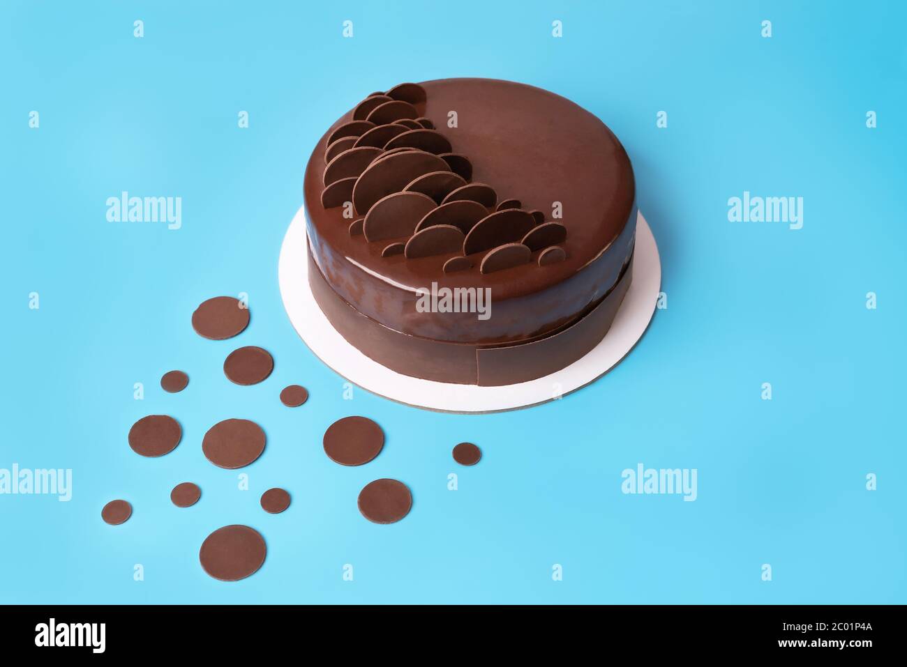 Dunkle Schokolade Mousse Kuchen mit Spiegelglasur bedeckt und mit runden Schokoladenstückchen auf blauem Hintergrund dekoriert. Moderner, stilvoller Kuchen. Nahaufnahme. Kopieren Stockfoto