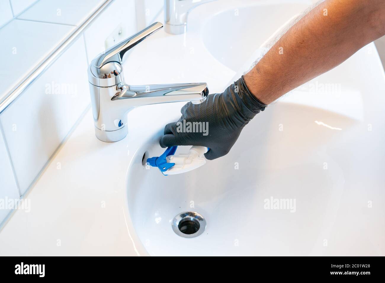Ein Mann, der das Waschbecken in einem Badezimmer mit einer Sprühflasche und anderen Reinigungsgeräten reinigt Stockfoto