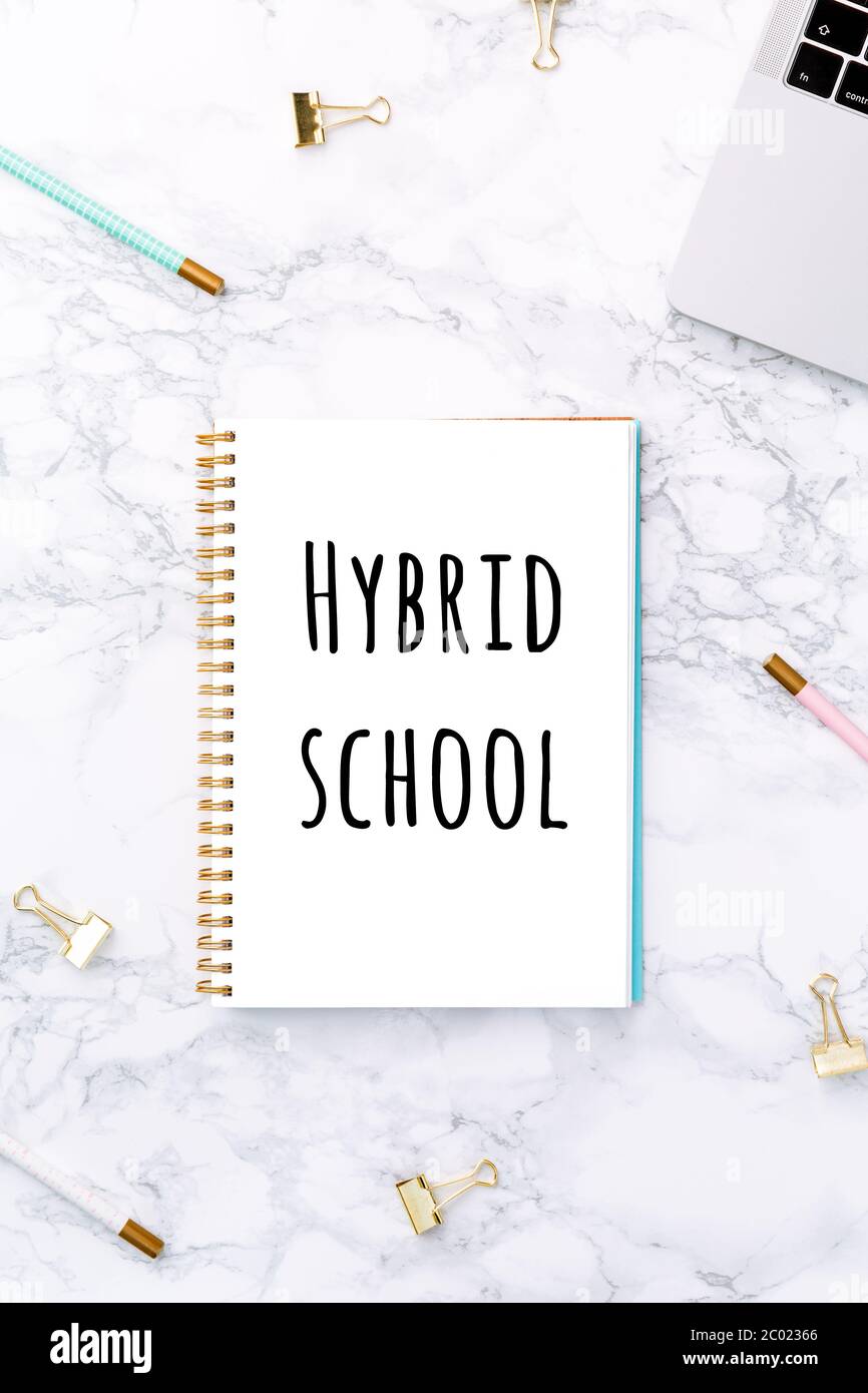 Notizblock mit Hybrid-Schulschrift, Laptop und festlicher goldener Schreibwaren auf weißem Marmorgrund. Schulbildung neu gestaltet durch Coronavirus Konzept. Draufsicht. Vertikal Stockfoto