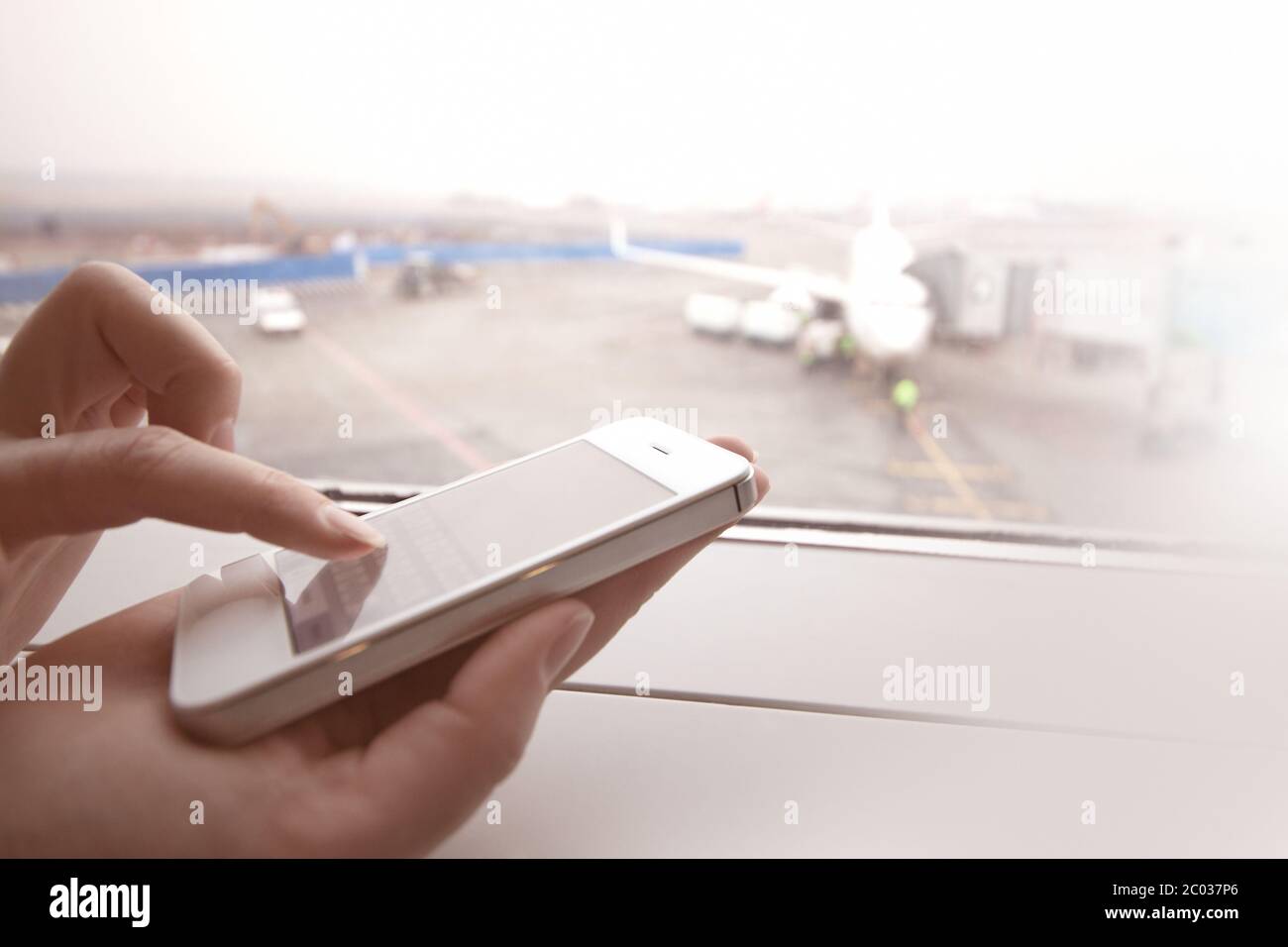 Frau mit Smartphone durch das Fenster am Flughafen Stockfoto