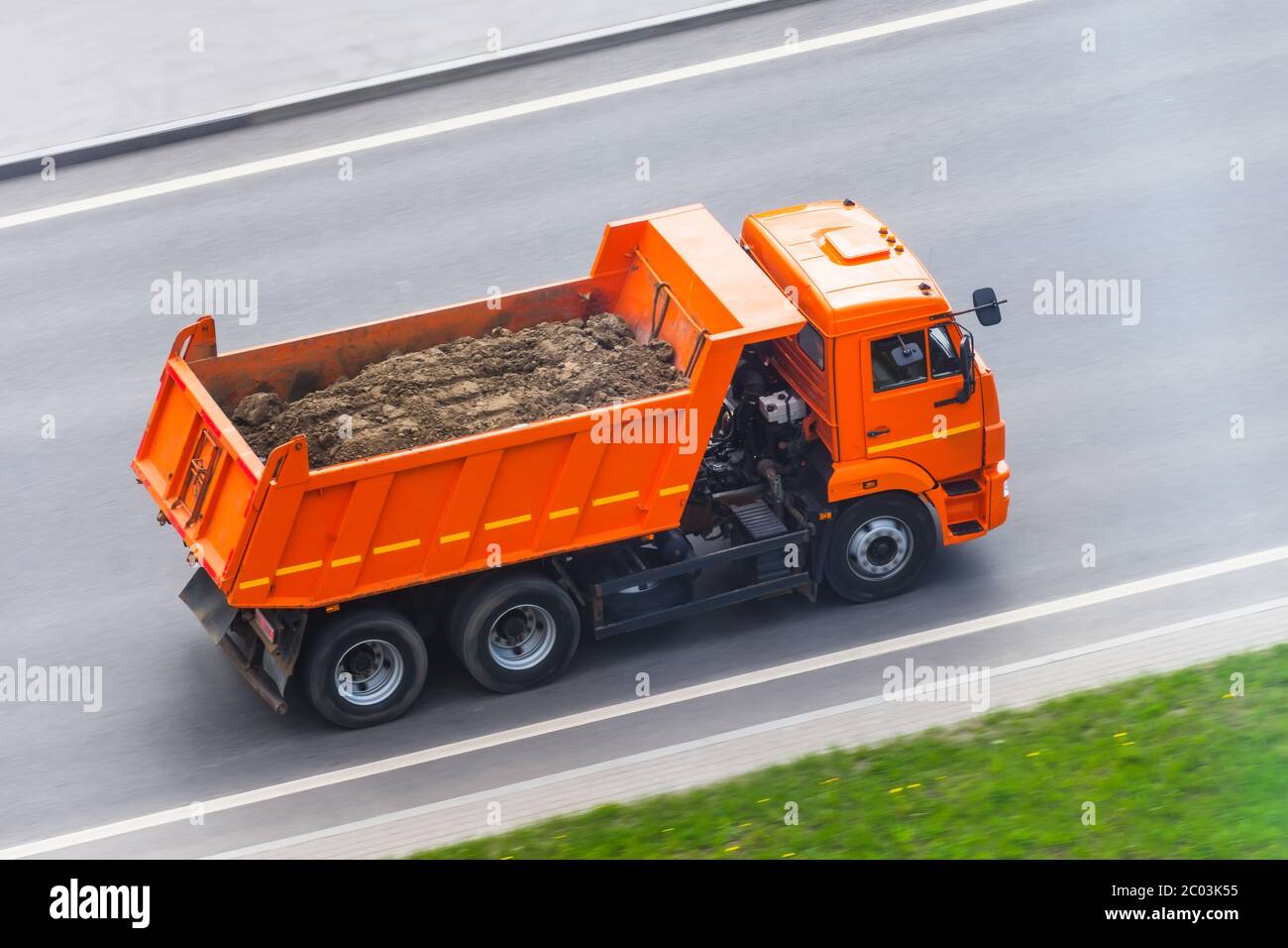 Orange LKW-Kippe mit einer Ladung Erde in der Karosserie fährt auf der Autobahn Stockfoto