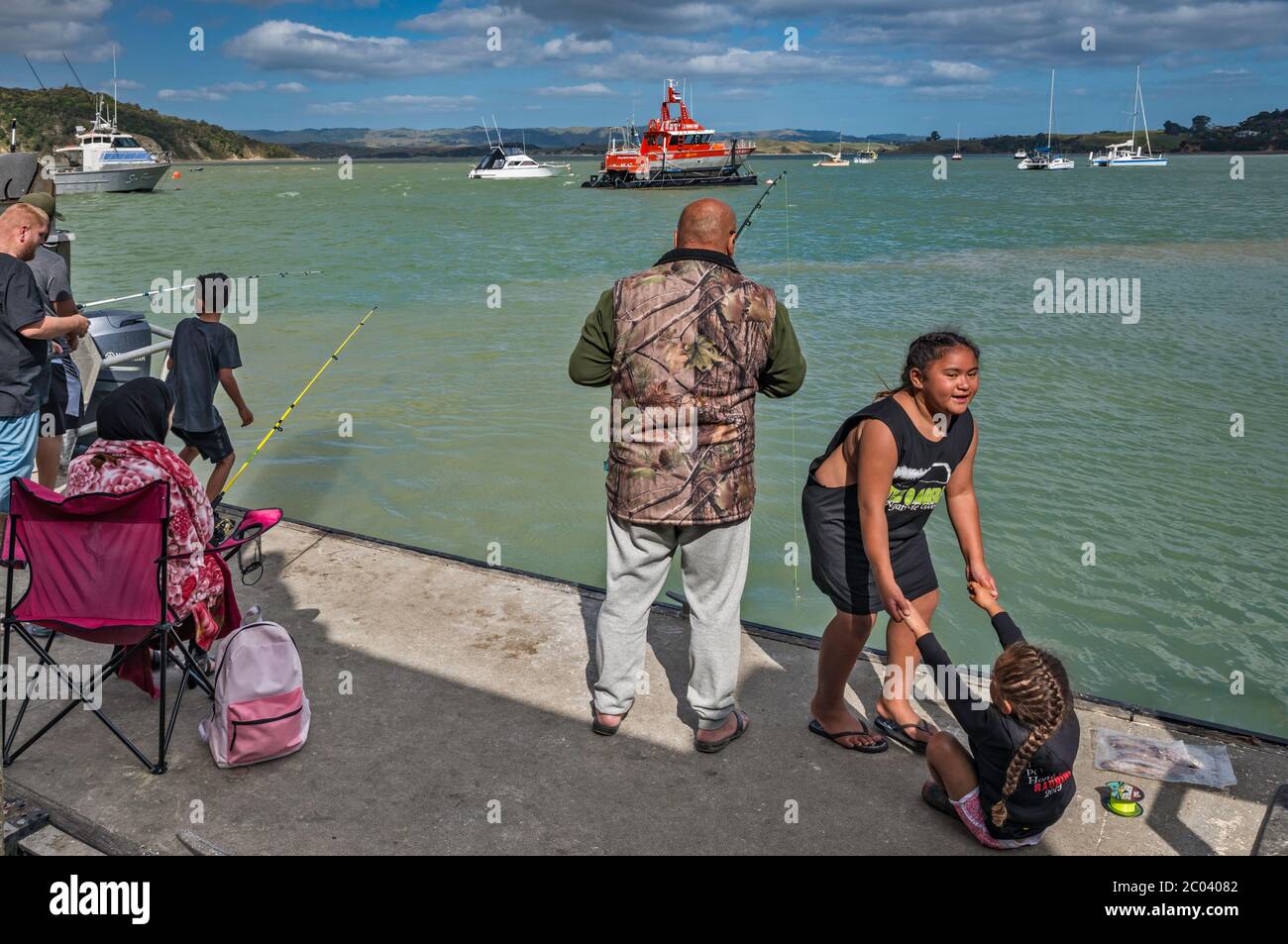 Leute angeln, Kinder spielen in Raglan Wharf über Cox Bay in Raglan, Waikato Region, North Island, Neuseeland Stockfoto