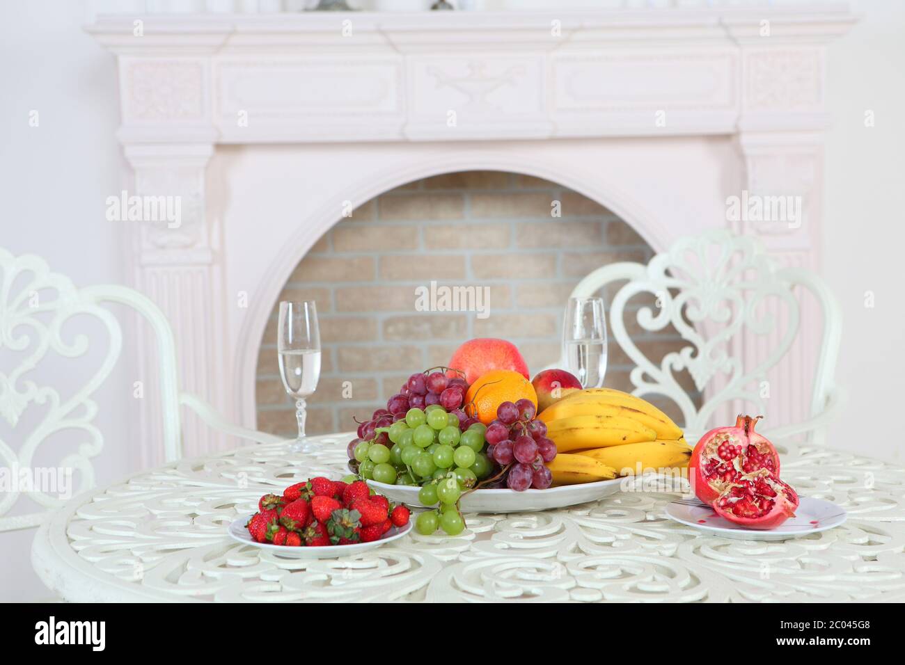 Erdbeere, Granatapfel, Trauben, Bananen, Orange und Apfel und Gläser mit Wasser auf einem weißen Tisch Stockfoto