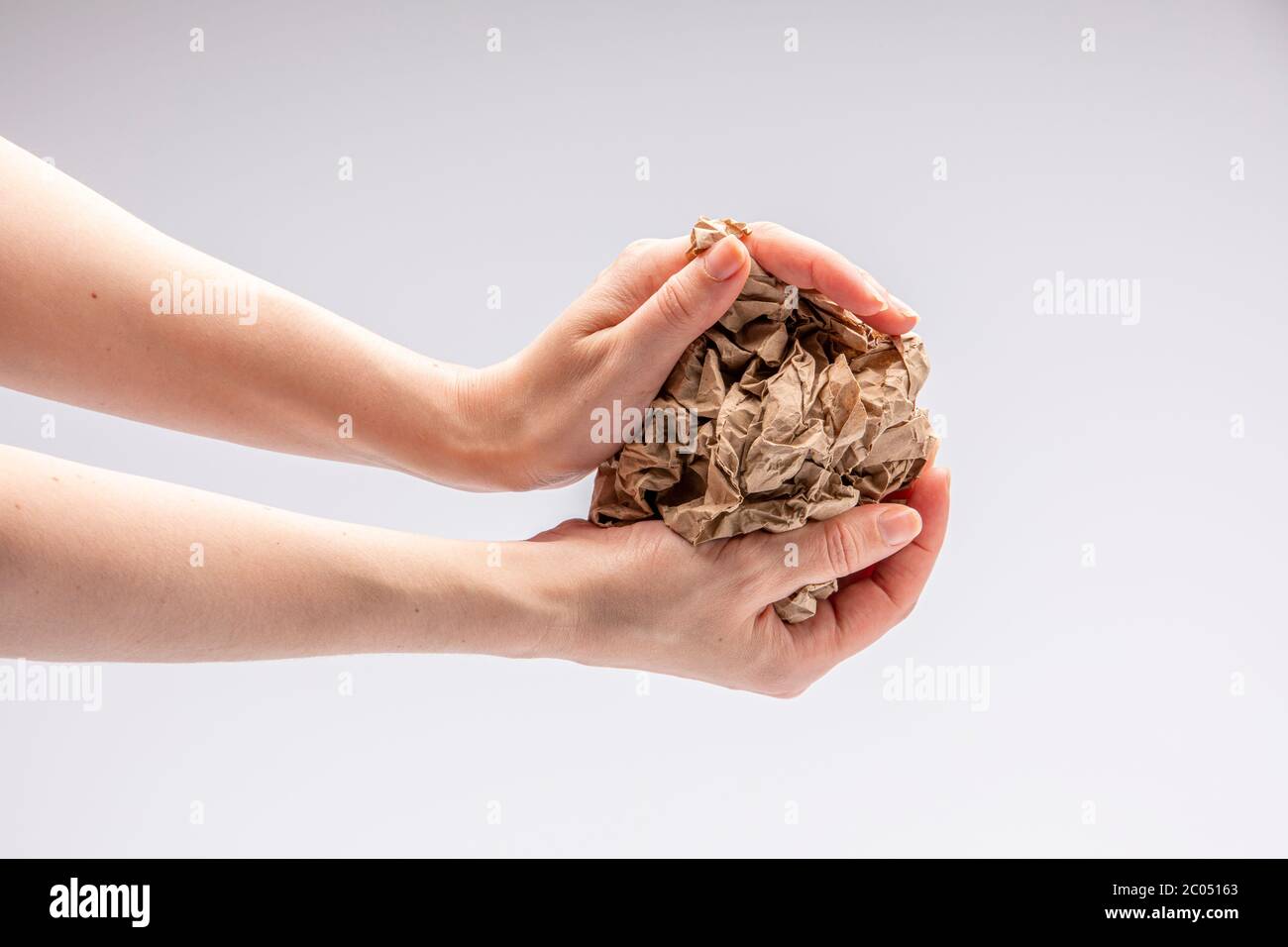 Nahaufnahme einer weißen Menschenhand, die ein zerknittertes Stück braunes Papier vor einem weißen Hintergrund hält Stockfoto